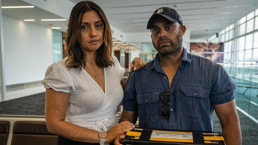 Greg Jenkins holds a box with his mother's ashes at Adelaide Airport