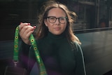 A young white woman with long brown hair standing int he street. She's holding a bright green lanyard with sunflowers on it