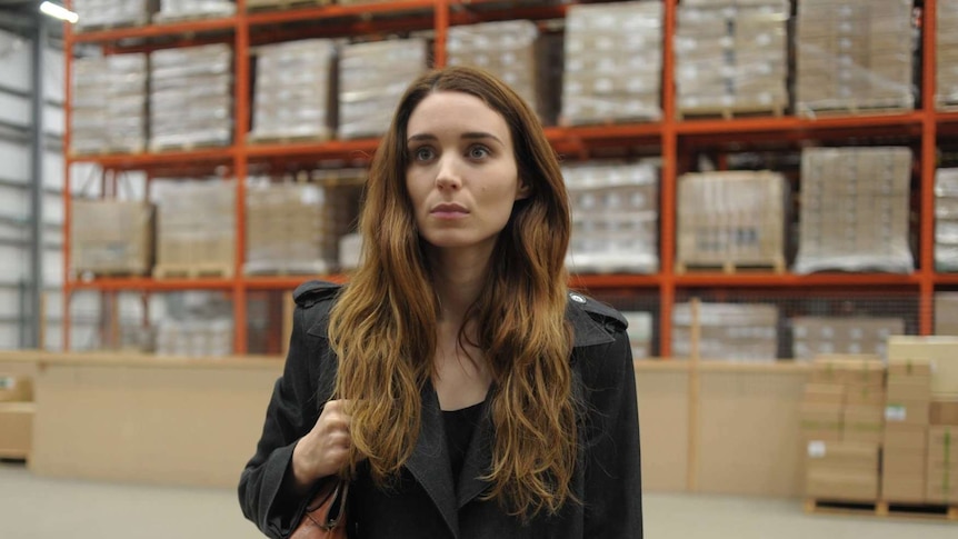 In a packing warehouse, Mara's character stares off camera.