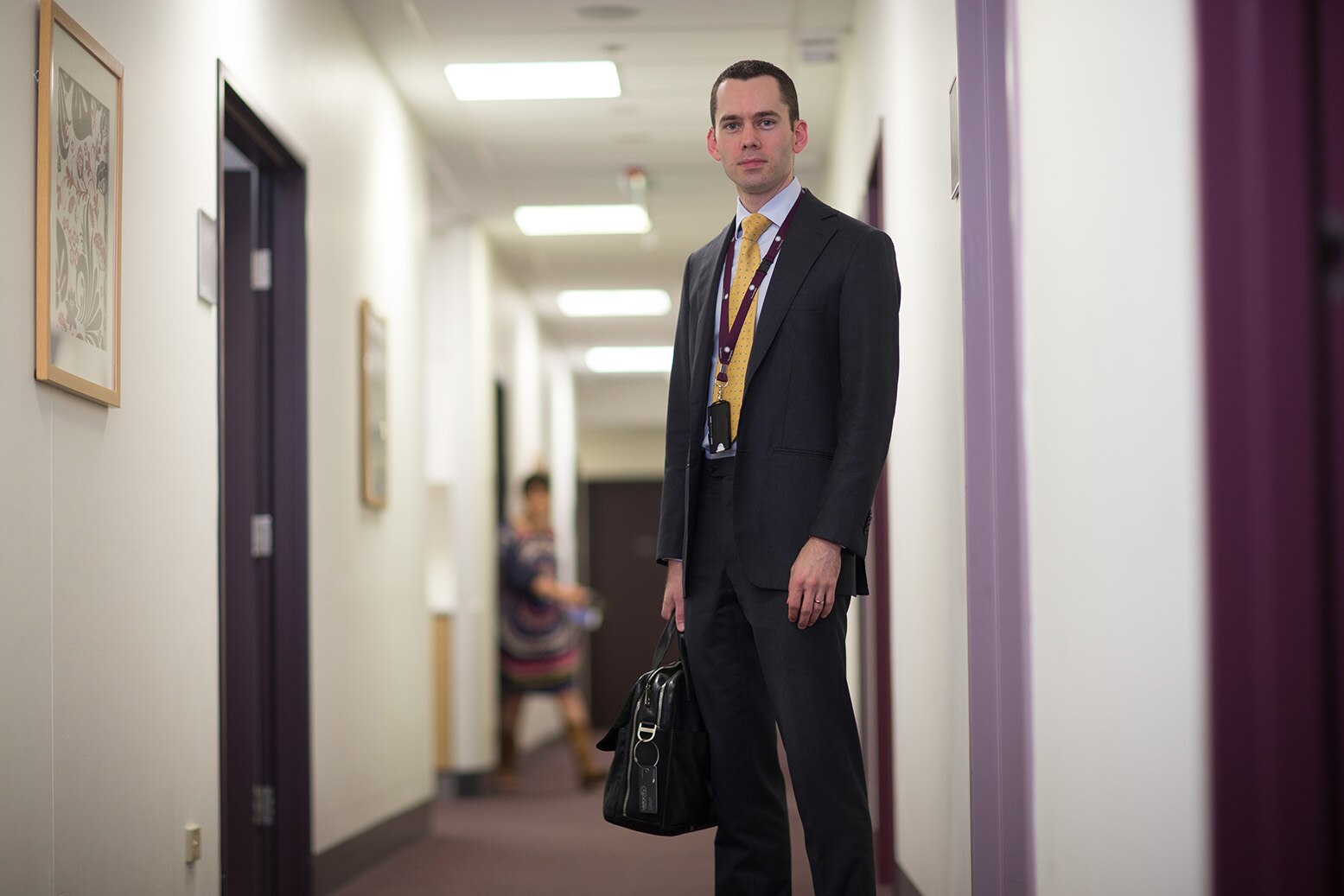 A young male doctor in a suit stands in a hall with a briefcase