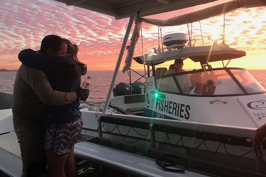 John Craig hugs his wife while standing on the deck of a boat.