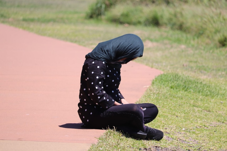 A girl sits cross-legged on a path looking down