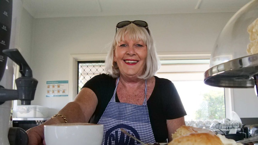 A blonde lady in a CWA apron serves scones.
