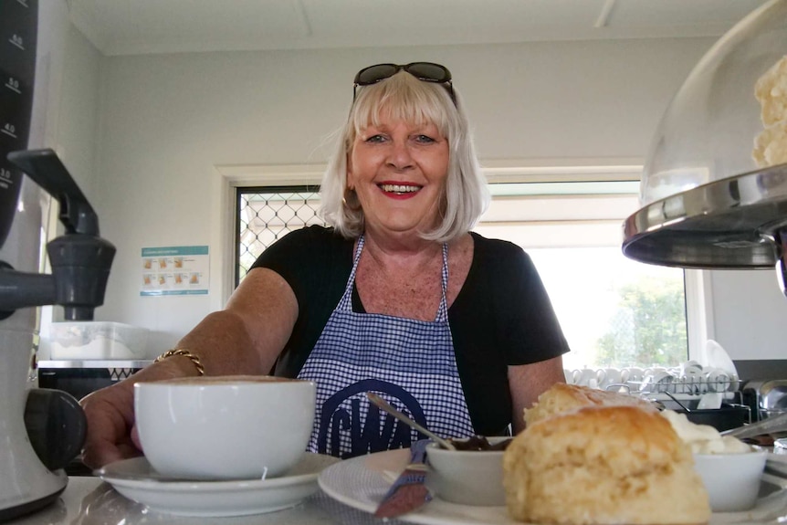 A blonde lady in a CWA apron serves scones.