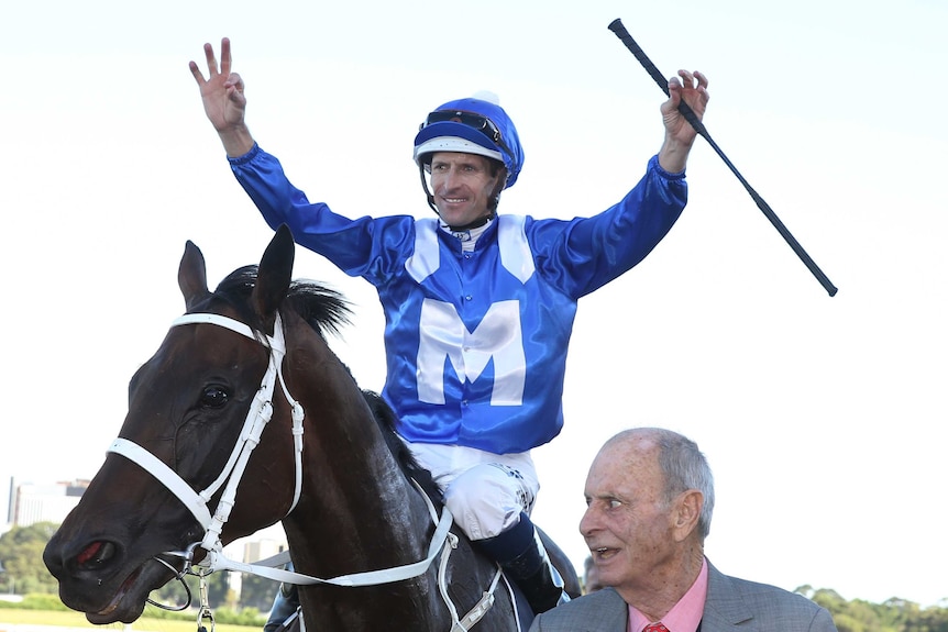 Jockey Hugh Bowman raises his arms in triumph after guiding Winx to her 17th straight victory.