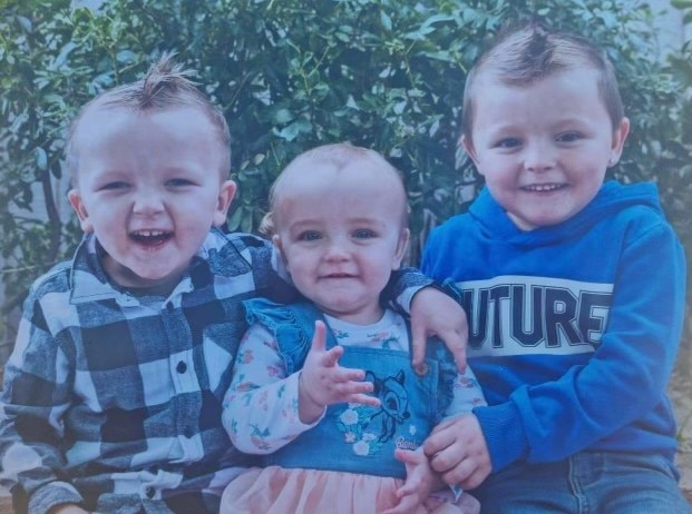 Toddlers Saige, Ashlynn and Isaac sitting next to each other smiling