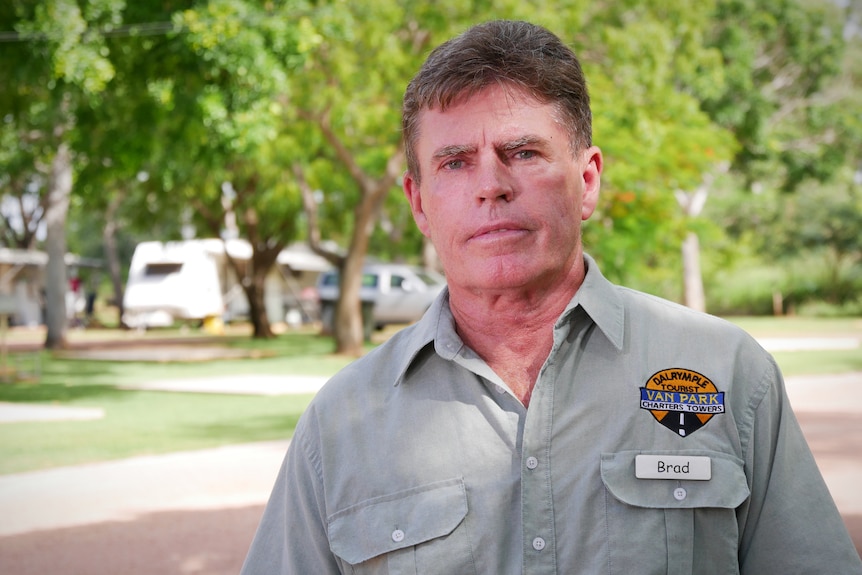 A man in a khaki shirt stands in front of a park with caravans