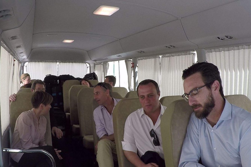Six politicians chat as they sit on a mini bus through the middle-east
