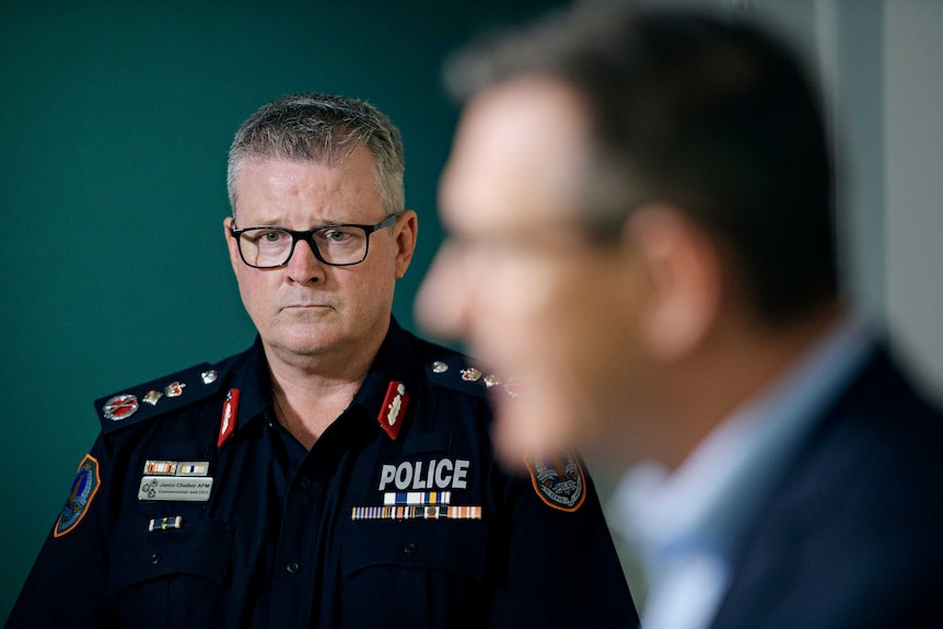Jamie Chalker looks worried as NT Chief Minister Michael Gunner, blurry, speaks.