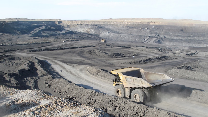 A large dump truck drives through an open-cut coal mine.