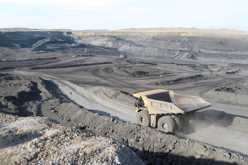 A large dump truck drives through an open-cut coal mine.