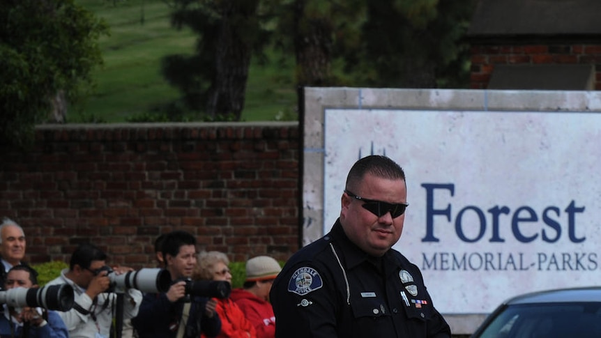 Members of the media and a police officer outside the Forest Lawn Memorial Park