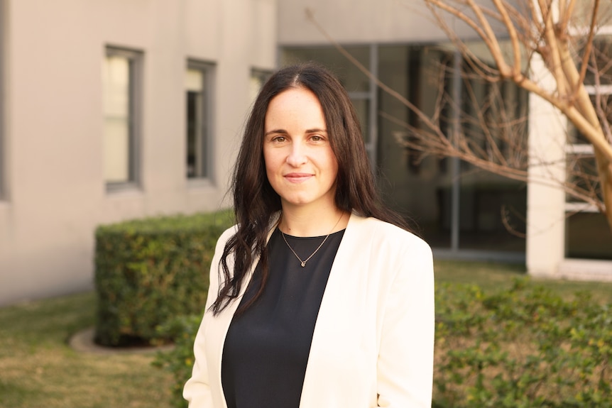 A young woman with dark hair wearing a black shirt and white blazer 