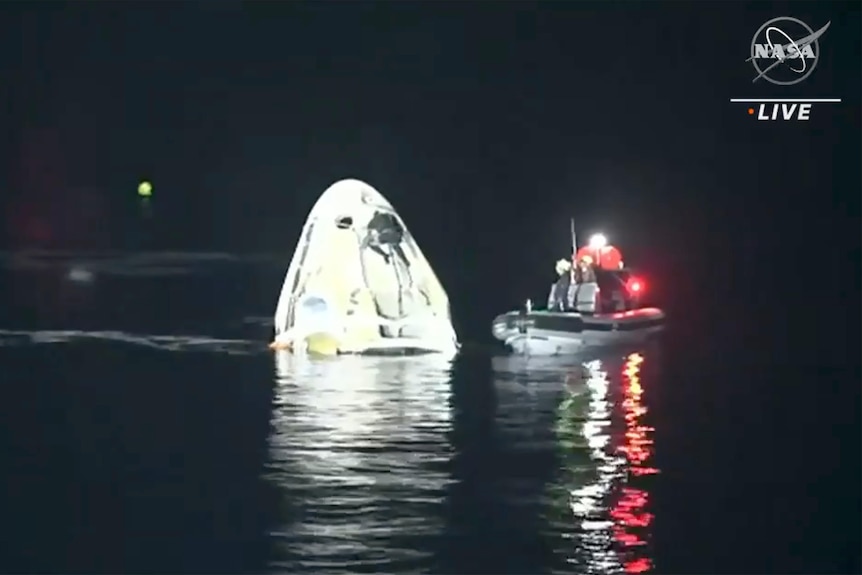 A space capsule and a boat in open water at night.