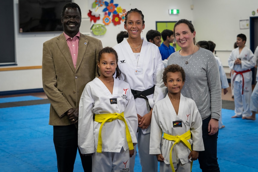 A family of five stands together smiling at the camera. The children are wearing taekwondo uniforms