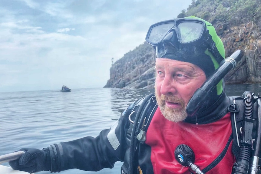 An older man in a dive suit and mask exiting the water.