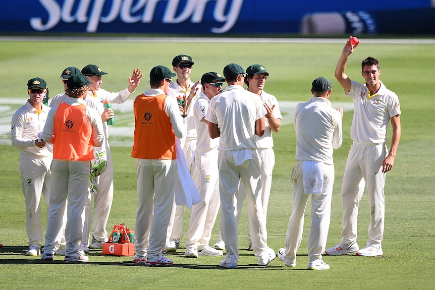 Pat Cummins raises the pink ball as his team-mates applaud.