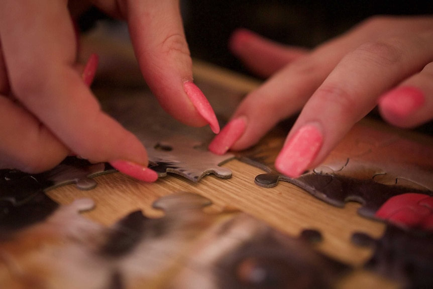 A hand with long nails puts a piece in a puzzle.