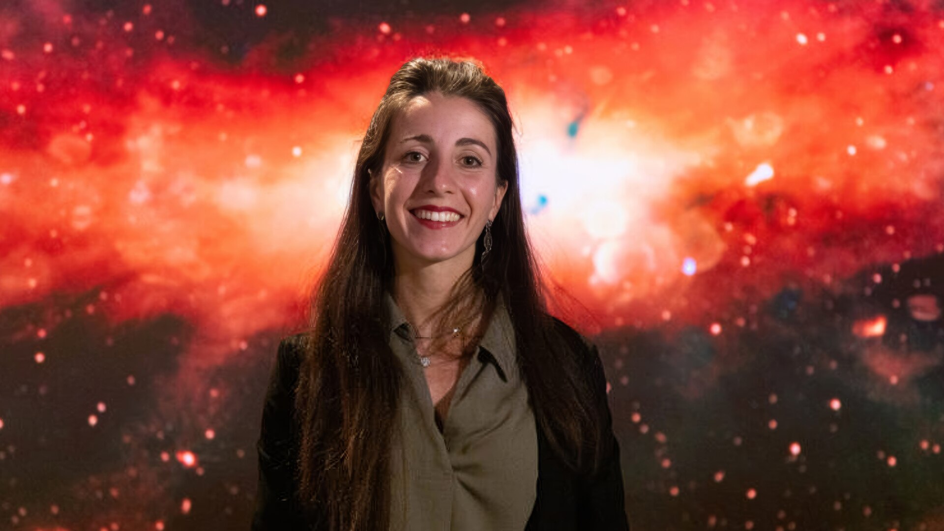 Silvia is smiling and standing in front of a red glowing Milky Way.