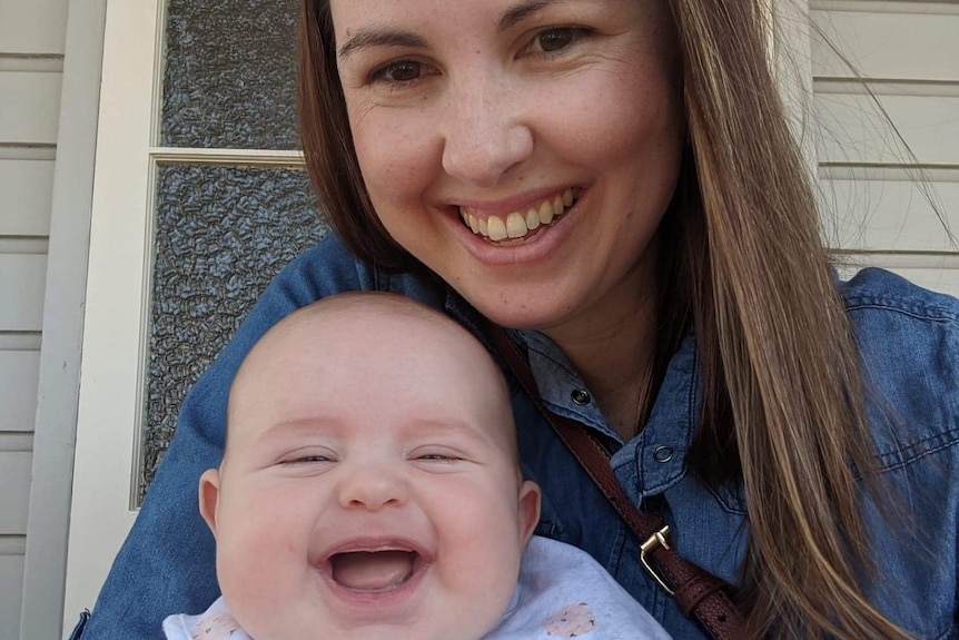 Caucasian woman sits with her baby boy on her lap, both joyfully smiling to the camera.