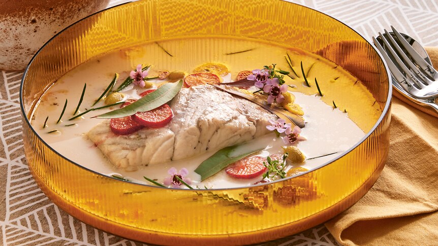 Poached barramundi in the yellow bowl with creamy sauce on a well set table.