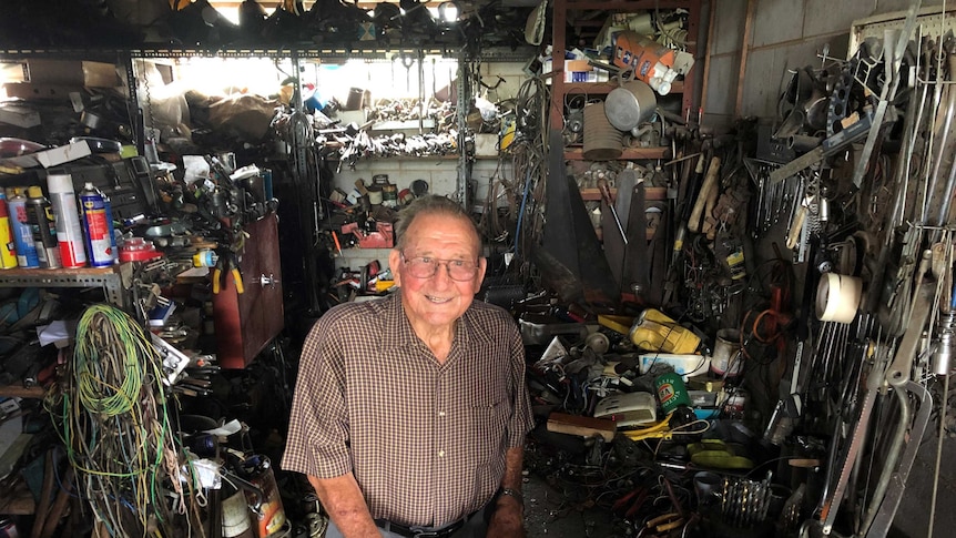 An elderly man stands in his workshop surrounded by an astonishing collection of tools, implements and useful bits and pieces
