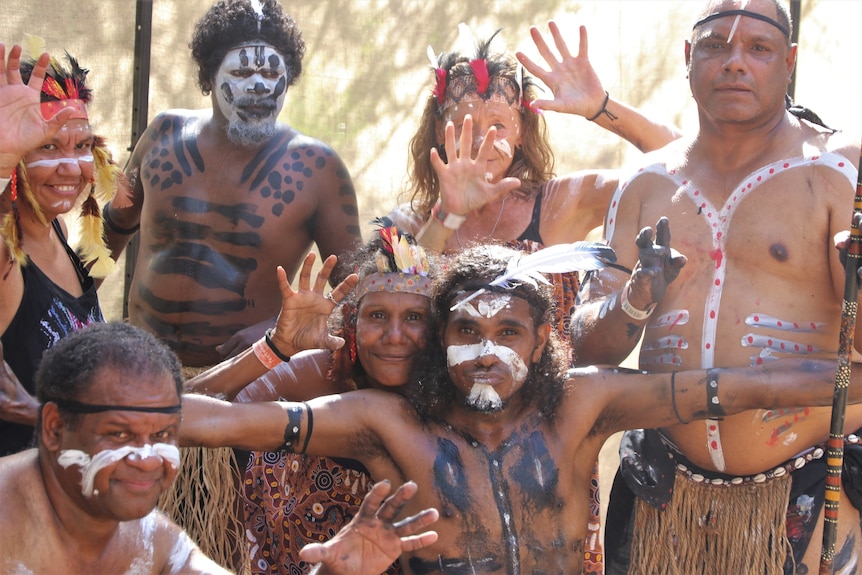 Group of Indigenous dancer wearing white and black paint and feather headress take a photo.