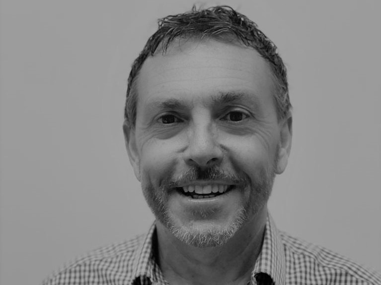 A black and white corporate headshot of a man smiling.