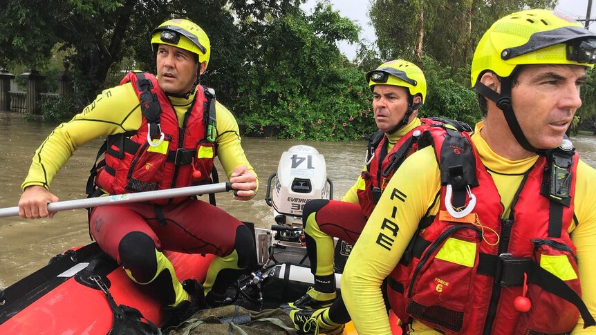 Three firefighters in lifejackets in an inflatable dinghy in floodwaters in Townsville.