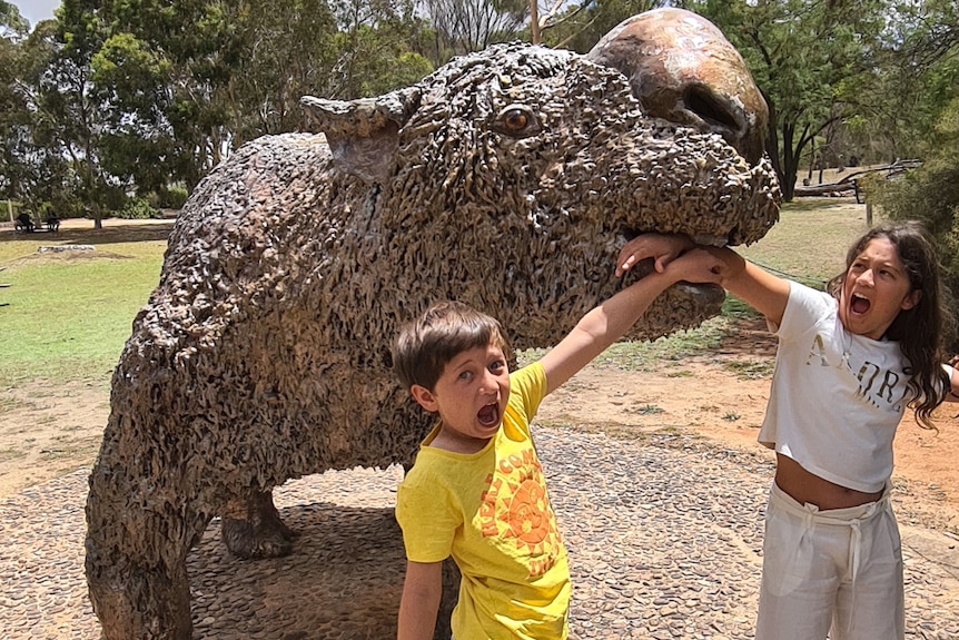 Two kids pretending to be eaten by a megafauna statue