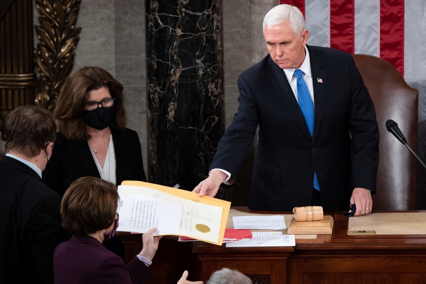 Mike Pence hands a document to a woman on the other side of his desk