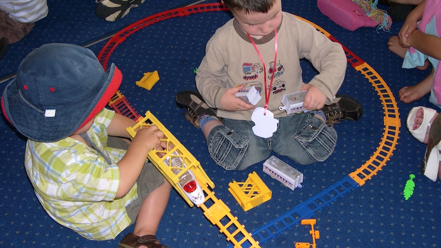 Two unidentified boys playing with trains on floor at child care centre.