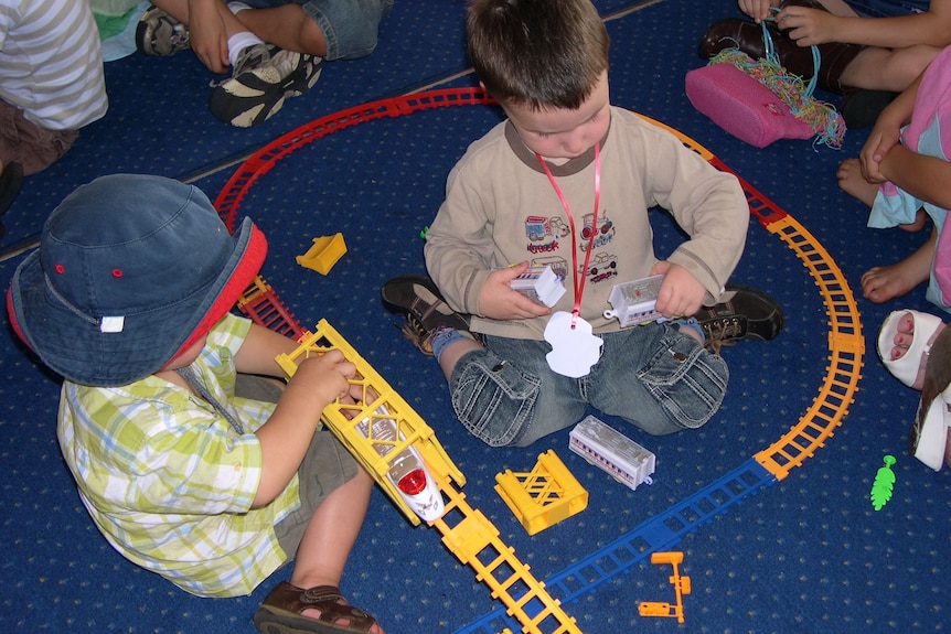 Two unidentified boys playing with trains on floor at child care centre.