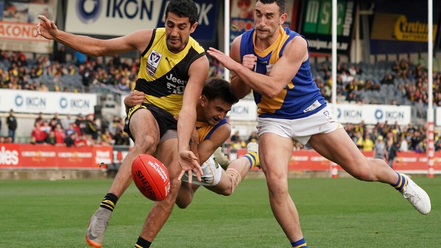 Marlion Pickett kicks the ball under pressure from two players in blue and yellow singlets