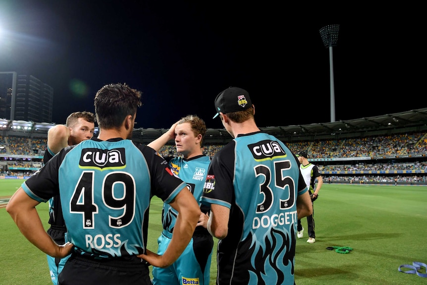 Brisbane Heat players stand on the Gabba turf after a Big Bash League game. The ground's lights are not working.