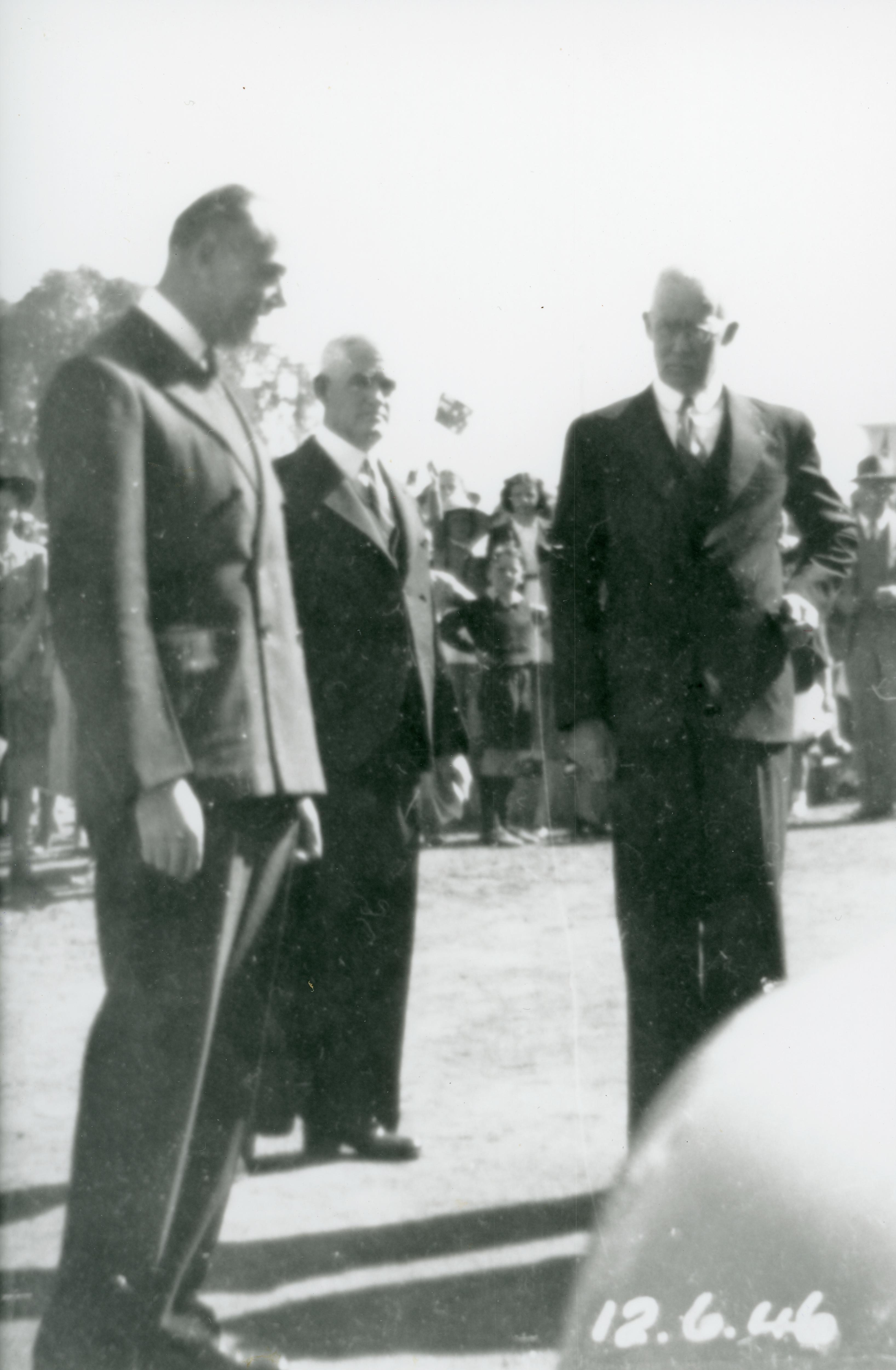 Black and white of three men in suits with crowd in background, vertical