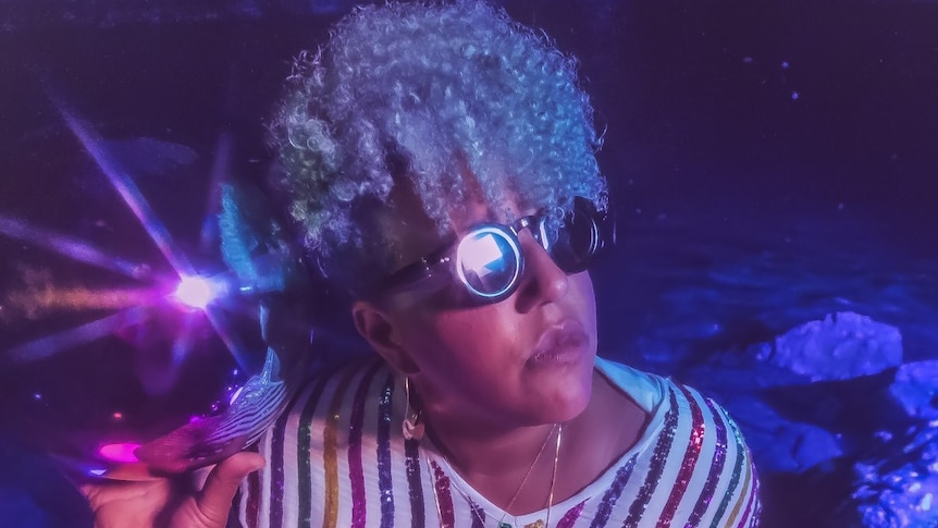 Brittany Howard holds a shiny ball that has light reflecting off it. She wears round sunglasses and a striped top.