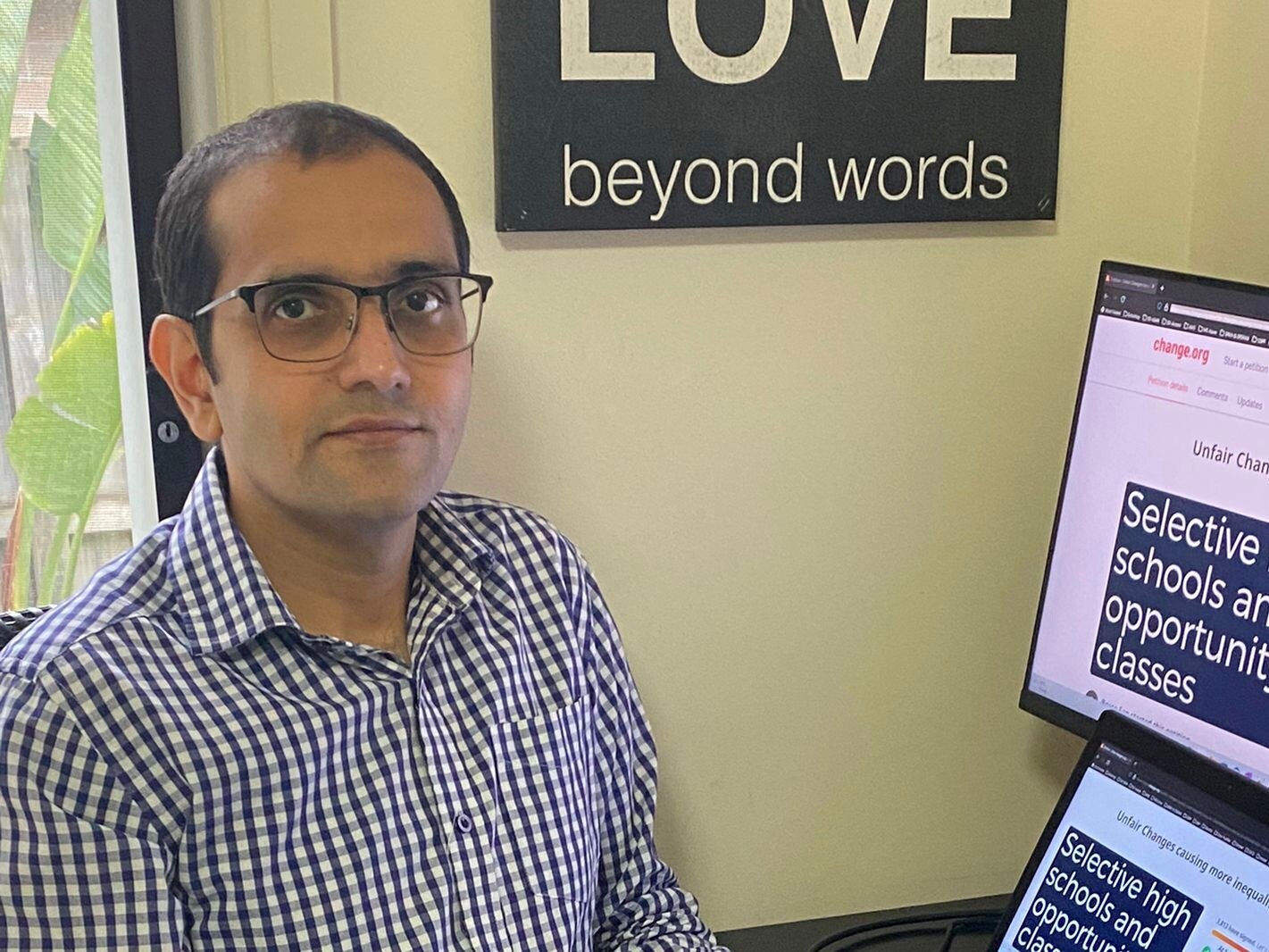 An Indian man with glasses sits next to his computer