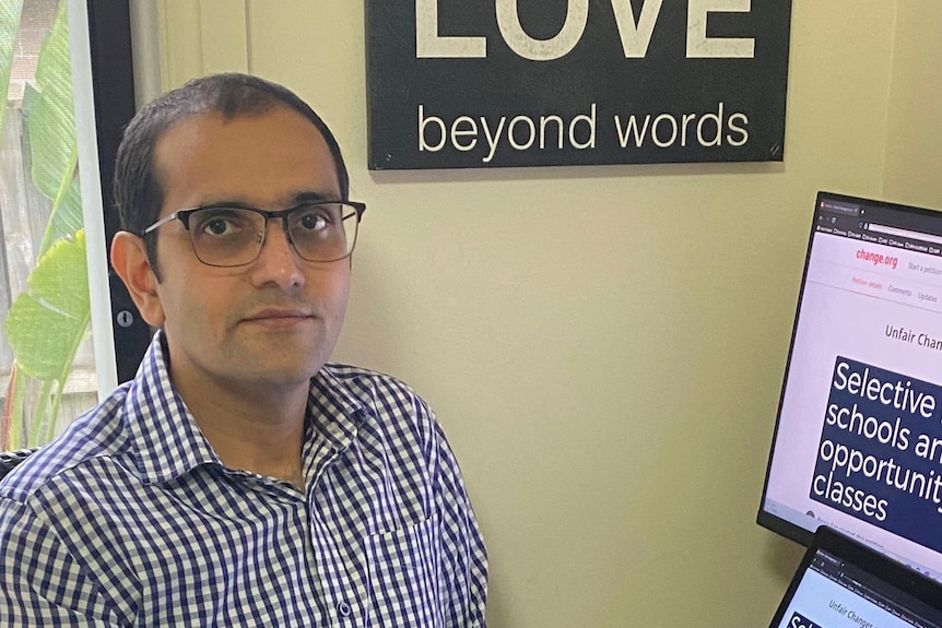 An Indian man with glasses sits next to his computer