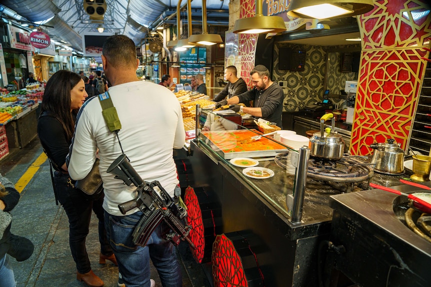 Diners, one of whom has a automatic rifle slung over his back, wait to be served at a counter in a restaurant.