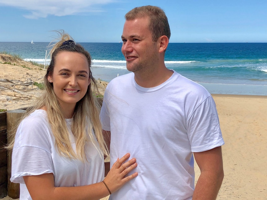 A couple standing on the beach smiling.