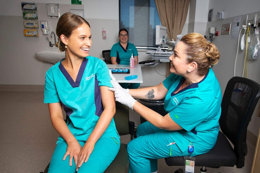 Zoe Park smiles at Kellie Kenway as she receives the first vaccine.