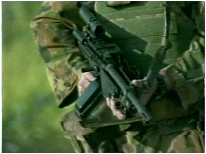 A still from a TV report showing a close up of a soldier's hands holding a rifle in East Timor.