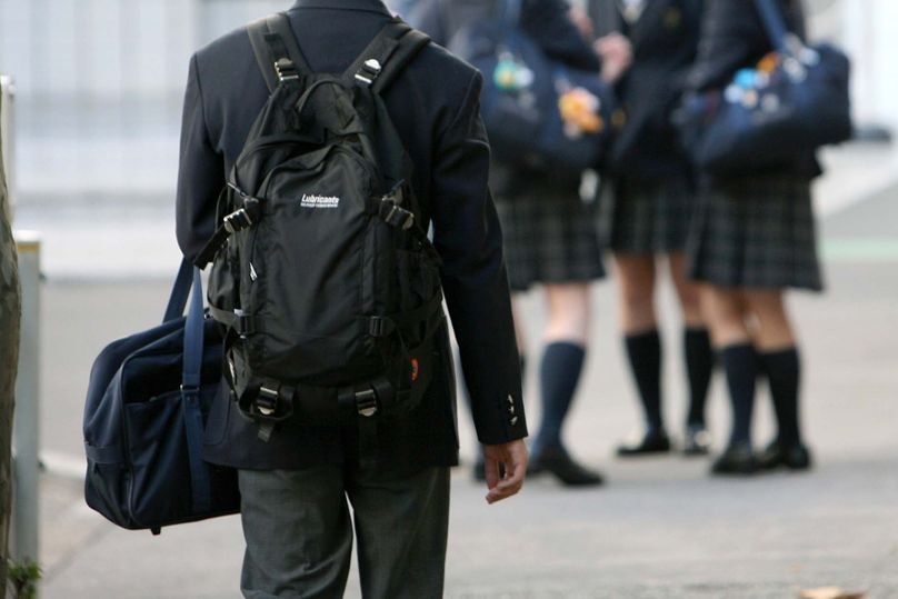 School student in uniform wearing a backpack walking toward a group of female students.