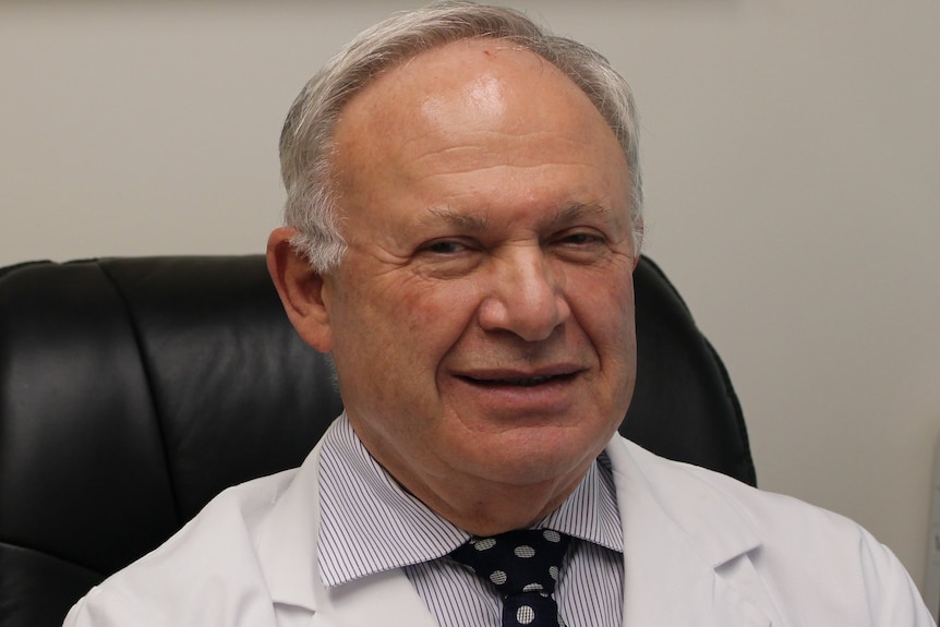 Dr Ronald Feiner smiles for a picture in  his white labcoat and tie 