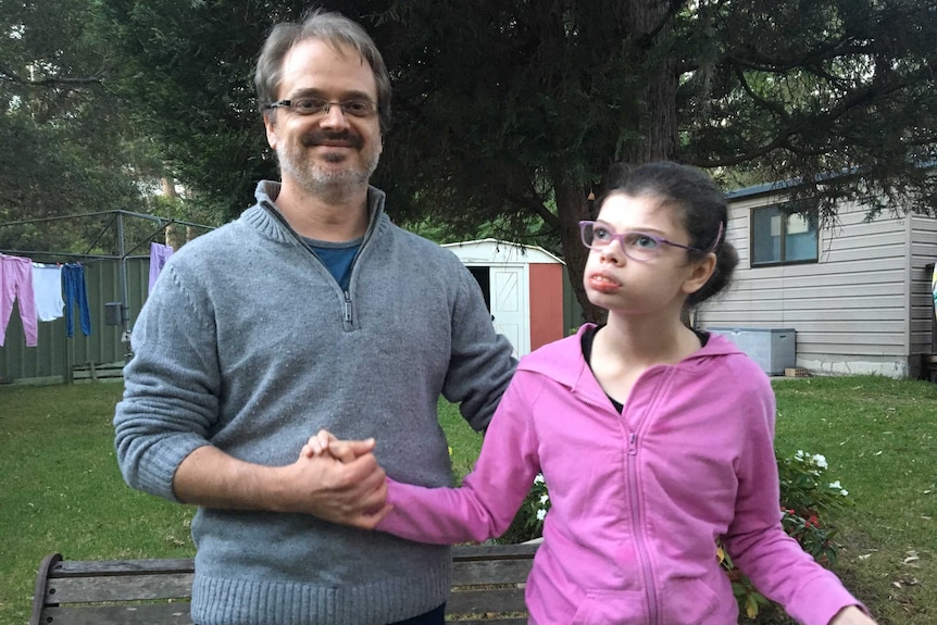 A father puts his arm around his daughter. They are sitting in a backyard, with a Hill's Hoist washing line in the background.