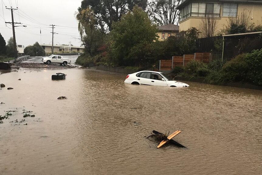 White car stranded in brown muddy floodwater.