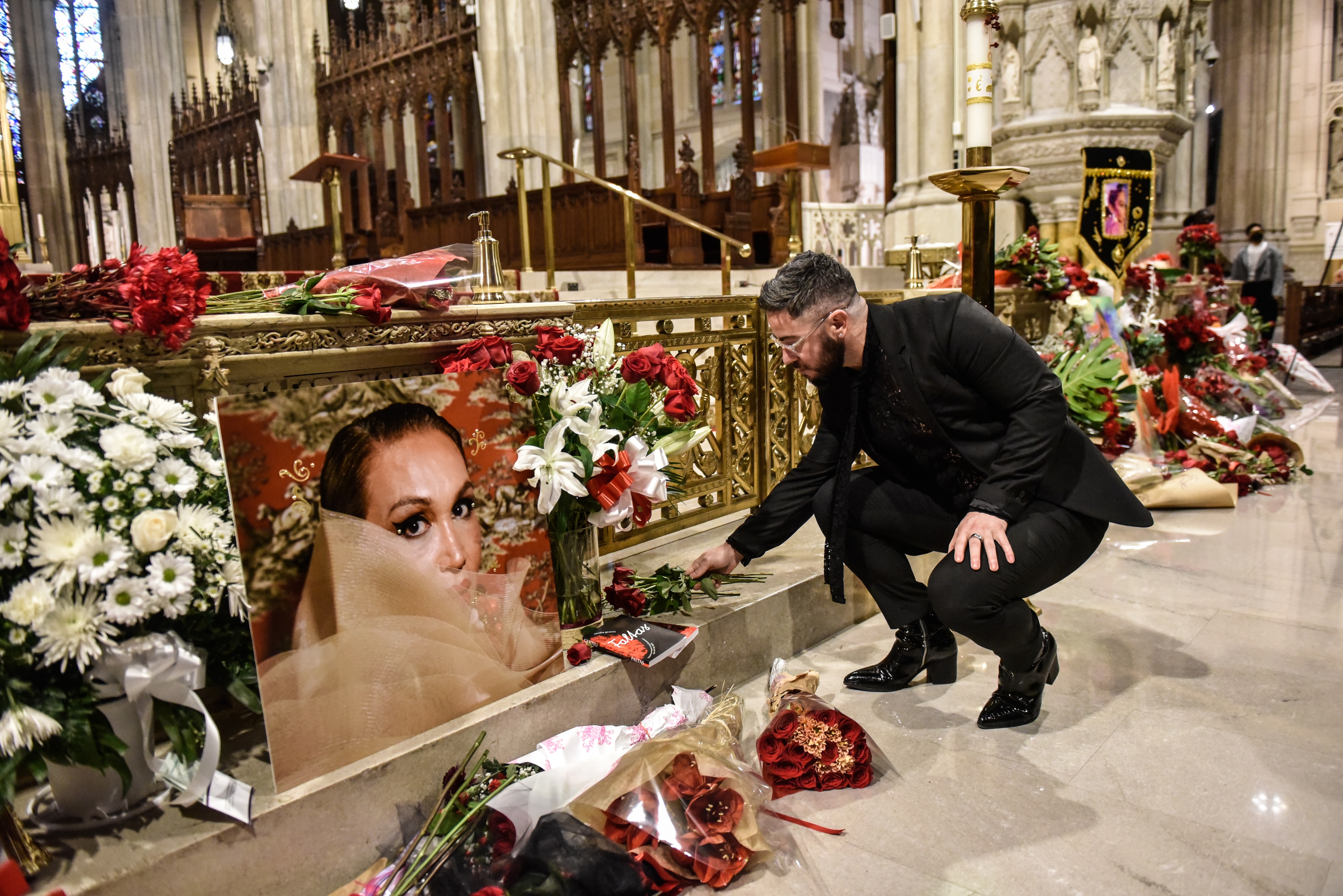 A person bends down to leave flowers next to an image of a woman surrounded by other flowers at the front of a church