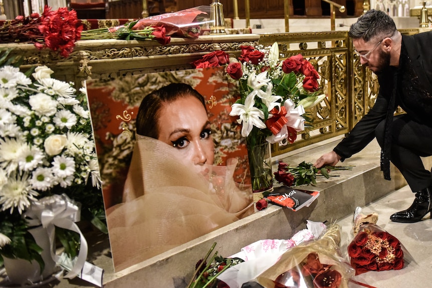 A person bends down to leave flowers next to an image of a woman surrounded by other flowers at the front of a church