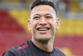 Israel Folau wears a red and black uniform on a field and stares off camera with a smile on his face.